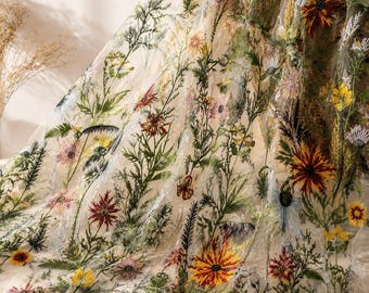 May include: A sheer, off-white fabric featuring intricate, multi-colored floral embroidery. The design showcases a variety of wildflowers, including red, yellow, and pink blossoms with green stems and leaves, scattered across the translucent material.