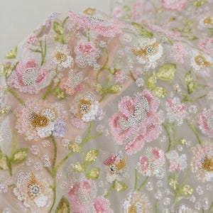Könnte beinhalten: Transparenter Stoff mit aufwendiger Blumenstickerei aus rosa, weißen und goldenen Pailletten und Perlen. Das Design zeigt detaillierte Blüten und grüne gestickte Stängel auf einem durchscheinenden, leichten Netzstoff als Basis.