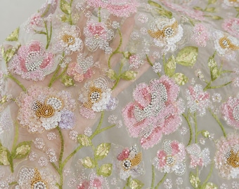 May include: Sheer fabric featuring intricate floral embroidery with pink, white, and gold sequins and beads. The design showcases detailed flower blossoms and green embroidered stems on a translucent, lightweight mesh base material.