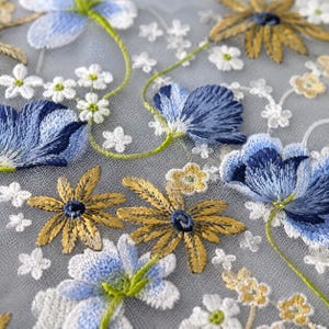 May include: A sheer grey mesh fabric featuring intricate embroidery of blue and white flowers, golden yellow daisy-like blossoms, and thin green stems. The floral pattern is densely arranged across the translucent material with detailed stitching.