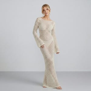 May include: A floor-length, cream-colored crochet dress featuring long, flared sleeves and a round neckline. The garment is constructed with an open-knit, repeating geometric pattern throughout, extending from the shoulders down to the hemline.