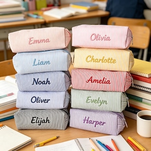 Può includere: Dieci astucci rettangolari a righe, ognuno con un nome ricamato unico sulla parte anteriore. Gli astucci sono disposti in due colonne e presentano vari colori pastello e vivaci, tra cui rosa, blu, giallo, rosso, verde e viola.