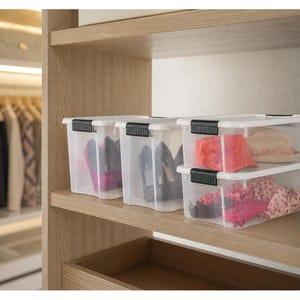 Puede incluir: Cajas de almacenamiento de plástico transparente con asas negras apiladas en un estante de madera. Las cajas contienen zapatos, sombreros y ropa. El estante del armario es de madera clara.