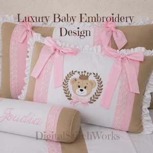 Peut inclure: Ensemble de literie pour bébé avec coussins brodés et un traversin. Les coussins sont beiges, blancs et roses, avec des nœuds et des bordures en dentelle. Le traversin est blanc avec une broderie rose. Le texte "Luxury Baby Embroidery Design" est visible.