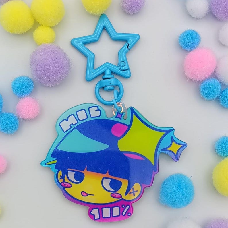 May include: A blue star-shaped keychain clip attached to a cartoon character charm. The charm features a blue-haired character with yellow skin, the word "MOG", and the text "100%" in a pink banner. Colourful pom-poms surround the keychain.