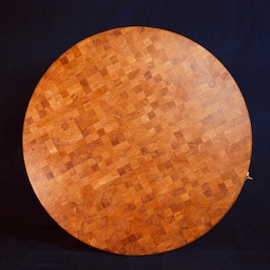 Peut inclure: Une planche à découper ronde en bois présentant une construction en bois de bout avec une mosaïque de petits blocs carrés de couleur brun clair et moyen. Les motifs du grain varient sur chaque bloc, créant une surface texturée.