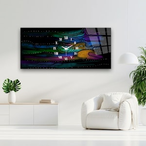 Pode incluir: Um relógio de parede retangular com fundo preto e faixas horizontais abstratas em azul, verde, roxo e laranja. O mostrador exibe algarismos romanos brancos de I a XII e ponteiros brancos centralizados no design.