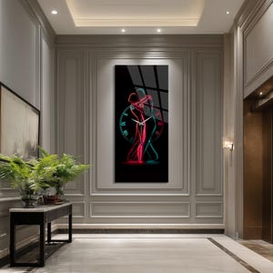 May include: A rectangular wall clock featuring a black background with a neon-style graphic of two figures dancing in red and blue outlines. The clock face includes Roman numerals arranged in a circle around the figures with white clock hands.