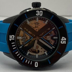 May include: A Ulysse Nardin wristwatch featuring a black case and a bright blue rubber strap. The dial is skeletonized, revealing internal gold-toned mechanical components, with a black X-shaped bridge, white hour markers, and blue accents.