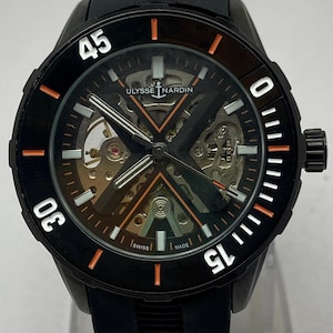 K&ouml;nnte beinhalten: Eine schwarze Ulysse Nardin Armbanduhr mit skelettiertem Zifferblatt, X-f&ouml;rmiger Br&uuml;cke, orangefarbenen Akzenten und wei&szlig;en Leuchtmarkierungen. Die Uhr verf&uuml;gt &uuml;ber eine schwarze Drehl&uuml;nette mit wei&szlig;en Ziffern und ein schwarzes Kautschukarmband.
