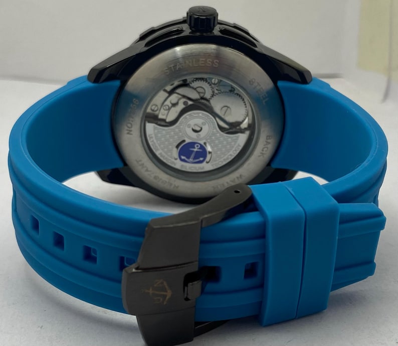 May include: A wristwatch with a bright blue silicone strap and a black buckle featuring an anchor logo. The watch case is black with a transparent exhibition case back revealing the internal mechanical movement and a small blue anchor emblem.