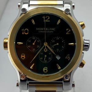 Może przedstawiać: Zegarek chronograf Montblanc z czarną tarczą, złotymi cyframi i złotymi wskaz&oacute;wkami. Zegarek posiada dwukolorową bransoletę ze stali nierdzewnej w kolorze srebrnym i złotym, złotą lunetę oraz trzy tarcze pomocnicze z datownikiem na godzinie czwartej.