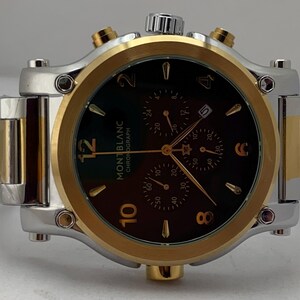 Może przedstawiać: Zegarek chronograf Montblanc z dwukolorową bransoletą i kopertą ze stali nierdzewnej w kolorze srebrnym i złotym. Ciemnobrązowa tarcza posiada złote cyfry na godzinach 12, 10, 8, 6, 4 i 2, trzy subtarcze, okienko datownika oraz złote wskaz&oacute;wki.