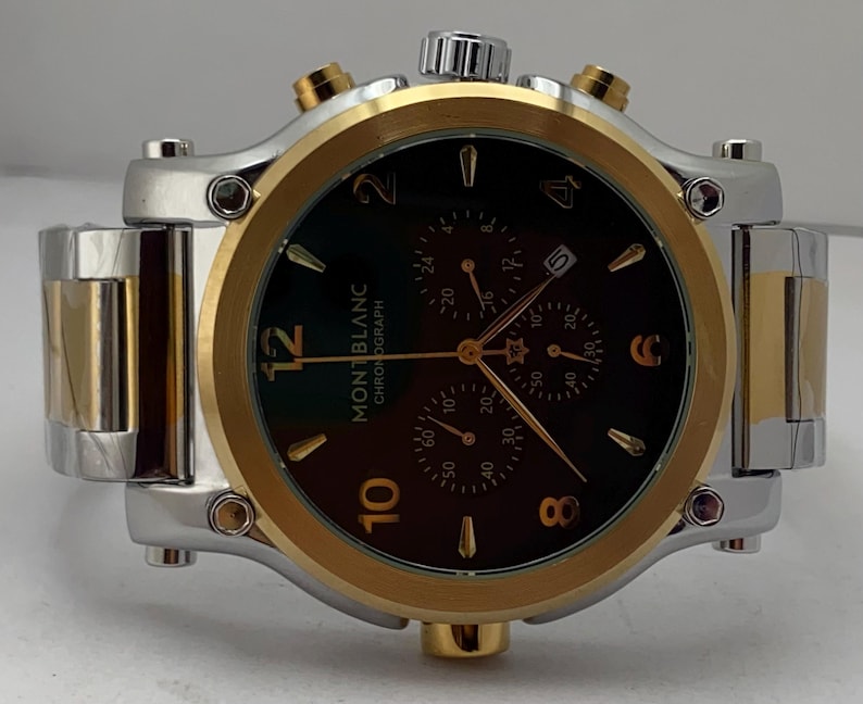 Może przedstawiać: Zegarek chronograf Montblanc z dwukolorową bransoletą i kopertą ze stali nierdzewnej w kolorze srebrnym i złotym. Ciemnobrązowa tarcza posiada złote cyfry na godzinach 12, 10, 8, 6, 4 i 2, trzy subtarcze, okienko datownika oraz złote wskaz&oacute;wki.