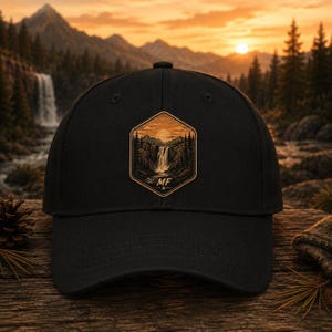 May include: A black baseball cap featuring a central hexagonal patch. The patch displays a detailed illustration of a waterfall, pine trees, and mountains under a setting sun, with the letters MF printed in a bold font at the bottom of the design.