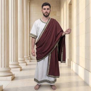 May include: A white tunic with short sleeves and a deep maroon toga draped over one shoulder. Both the tunic and the toga feature a decorative gold and black geometric trim along the edges. The garment reaches the ankles and has a loose fit.