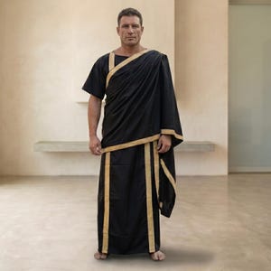 May include: A black floor-length tunic featuring a draped shoulder design and gold-colored trim along the neckline, across the chest, and down the front panels. The garment has short sleeves and a loose, flowing silhouette with structured fabric.