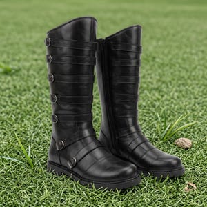 May include: A pair of black knee-high boots featuring a smooth finish, rounded toes, and multiple horizontal straps across the shaft. Each strap is secured with a silver-toned metal buckle, and a vertical zipper is visible on the inner side of the boots.