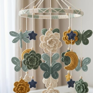 May include: A handmade crochet baby mobile featuring butterflies, flowers, stars, a dragonfly, and a crescent moon in shades of cream, yellow, blue, and green. The mobile is suspended from a circular frame with a cream and green striped design.