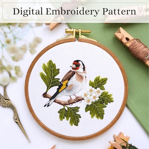 Könnte beinhalten: Ein runder Stickrahmen aus Holz mit weißem Stoff, auf dem ein detaillierter Stieglitz auf einem Ast mit grünen Blättern und weißen Blüten gestickt ist. Der Text Digital Embroidery Pattern ist oben im Bild zu sehen.