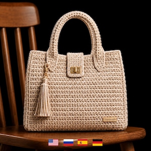 Op de afbeelding: Beige gehaakte handtas met een rechthoekige vorm en een handvat. De tas heeft een klepsluiting met een goudkleurige sluiting en een decoratieve kwast. Het woord "Handmade" staat op een klein houten label.