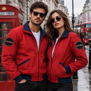 Puede incluir: Una chaqueta roja con cremallera, cuello, puños y dobladillo en azul marino. La chaqueta presenta un parche circular negro en la manga derecha con la palabra CUSTOMIZE en amarillo. Un parche circular negro idéntico con CUSTOMIZE está en la manga izquierda.