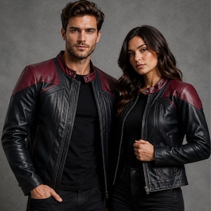 Puede incluir: Una chaqueta de cuero negra con paneles de color rojo oscuro en los hombros y el cuello, una cremallera frontal completa y detalles de costuras verticales. La chaqueta tiene un cuello alto con cierre de botón a presión y mangas largas.