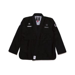 Könnte beinhalten: Eine schwarze Kampfkunst-Gi-Jacke mit langen Ärmeln und einem dicken Kragen. Auf der Brust befinden sich weiße gestickte Aufnäher mit dem Text VA, SHOYOROLL und RVCA. Das Innenfutter zeigt ein sich wiederholendes schwarz-weißes Grafikmuster.