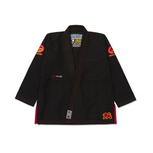 Puede incluir: Kimono de artes marciales negro con ribetes y detalles rojos. El kimono presenta logotipos bordados en las mangas y el pecho, y el texto "shoyoroll" es visible en el cuello. Diseñado para el entrenamiento y la competición de artes marciales.