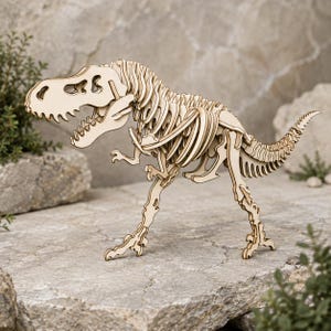 Op de afbeelding: Een lichtgekleurd houten model van een Tyrannosaurus Rex-skelet. De dinosaurusfiguur is opgebouwd uit in elkaar grijpende platte houten onderdelen, met een gedetailleerde ribbenkast, een grote schedel met open oogkassen en een lange, gesegmenteerde staart.