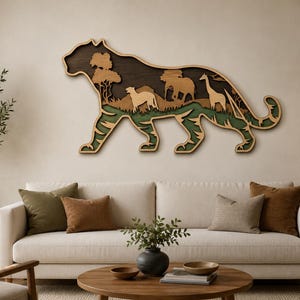 Peut inclure: Une décoration murale en bois multicouche en forme de silhouette de grand félin. L'intérieur présente des scènes découpées d'un paysage de savane avec un guépard, un éléphant et une girafe sur un fond brun foncé et un premier plan vert.