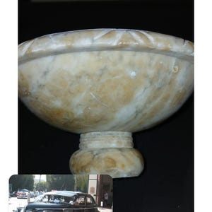 May include: A footed bowl crafted from polished stone with a marbled pattern in shades of cream, beige, and light brown. The bowl features a wide, rounded basin with a carved rim and a sturdy, circular pedestal base, showcasing natural veining.