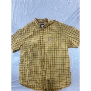 May include: A short-sleeve button-down shirt in a mustard yellow and brown plaid pattern. The shirt features a standard collar, a front button placket, and a single chest pocket with a small Columbia brand tag attached to the side of the pocket.