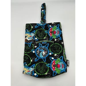 Könnte beinhalten: Schwarze, gesteppte Stofftasche mit einem sich wiederholenden Muster von Cartoon-Charakteren in Blau, Grün und Rot. Die Tasche hat einen Griff und ein rautenförmiges Steppmuster. Der Text "POCKET MONSTERS" ist sichtbar.