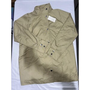 May include: A beige jacket with a high collar, long sleeves, and a button-up front. The jacket has a tag attached and appears to be made of a lightweight material. The jacket has a classic, versatile design.