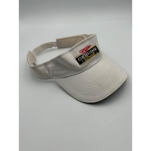 May include: A white visor featuring an embroidered Miller Genuine Draft logo on the front panel. The logo includes red, black, and gold text with two small stars. The visor has a curved brim and an adjustable hook-and-loop strap closure at the back.