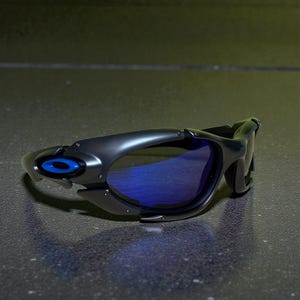May include: Black sunglasses with blue lenses. The sunglasses have a sleek, modern design with a matte finish. The frame features a blue accent on the side. The lenses are a vibrant blue color.