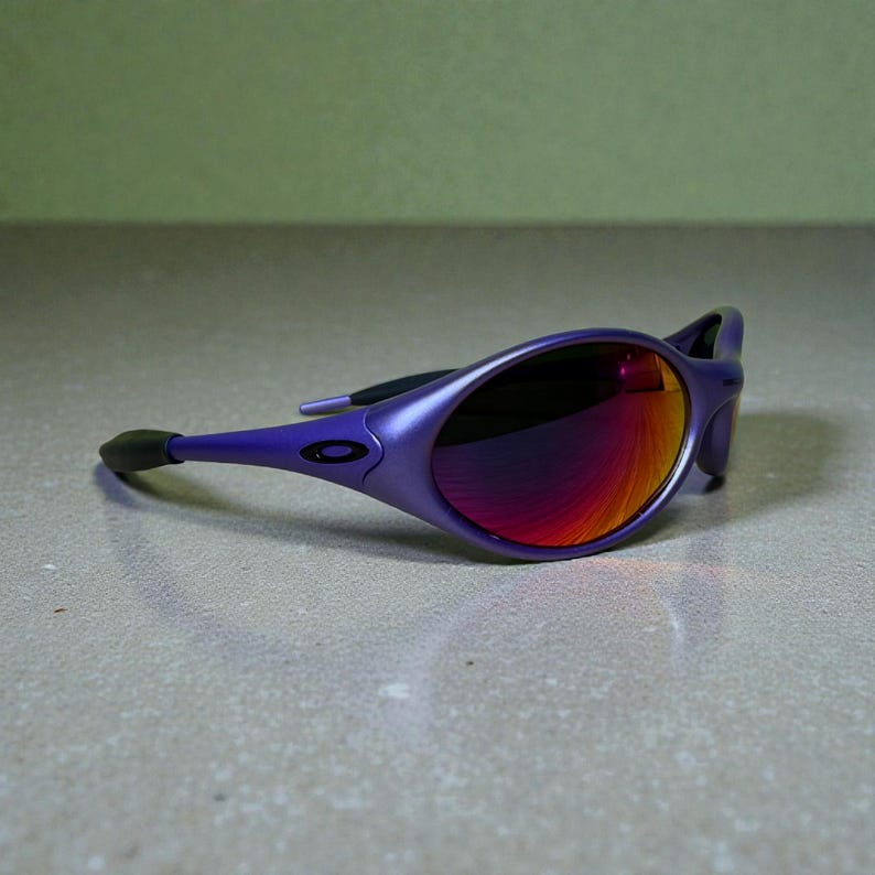 May include: Purple sunglasses with a sleek, oval frame and mirrored lenses that reflect shades of red and orange. The arms are a matching purple, with a black ear piece. The sunglasses are set against a neutral background.
