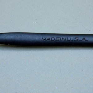 K&ouml;nnte beinhalten: Nahaufnahme eines schwarzen Objekts mit dem Text "MADEINU.S.A." in Wei&szlig;. Das Objekt scheint ein Schreibger&auml;t oder ein Werkzeug mit glatter, matter Oberfl&auml;che zu sein.