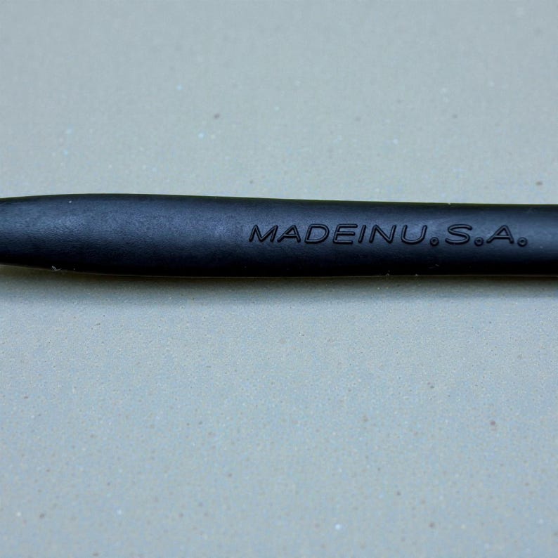 K&ouml;nnte beinhalten: Nahaufnahme eines schwarzen Objekts mit dem Text "MADEINU.S.A." in Wei&szlig;. Das Objekt scheint ein Schreibger&auml;t oder ein Werkzeug mit glatter, matter Oberfl&auml;che zu sein.