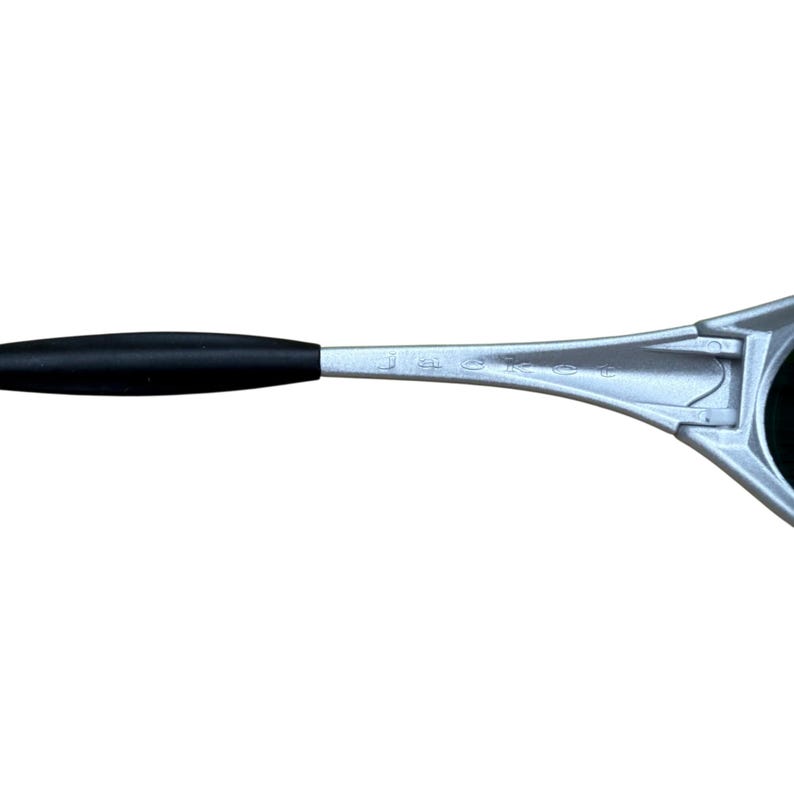 May include: Silver-framed sunglasses with a black arm. The sunglasses have a sleek, modern design. The lenses are dark, and the frame is a metallic silver color. The arm has a black rubber grip.