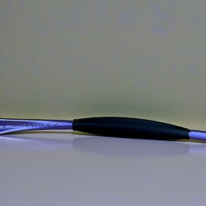 May include: A metal tool with a black rubber grip. The tool has a curved shape and is silver with the text "MADE IN USA" etched on the side. The background is a light beige color.