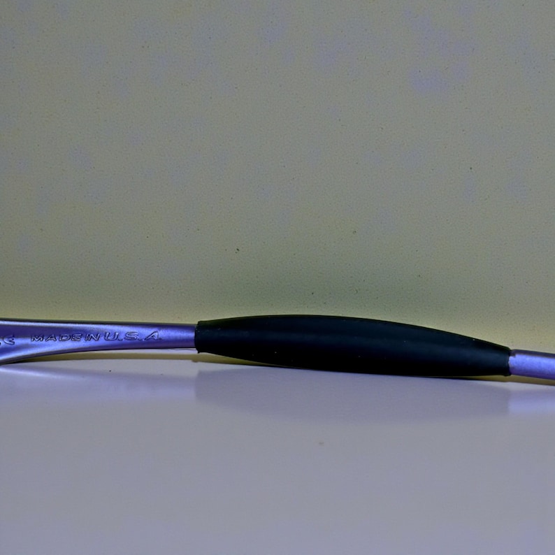 May include: A metal tool with a black rubber grip. The tool has a curved shape and is silver with the text "MADE IN USA" etched on the side. The background is a light beige color.