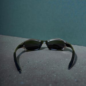 May include: A pair of sunglasses with a dark frame and lenses. The sunglasses have a sleek, modern design with curved arms and a metallic finish. The lenses are dark, providing shade and protection from the sun.