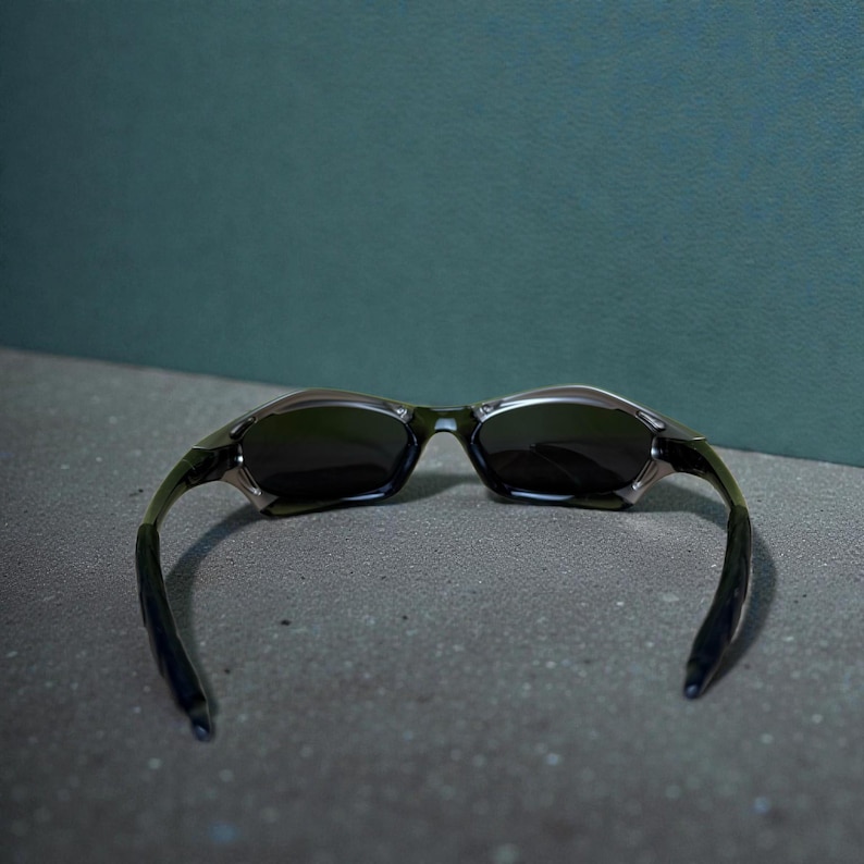 May include: A pair of sunglasses with a dark frame and lenses. The sunglasses have a sleek, modern design with curved arms and a metallic finish. The lenses are dark, providing shade and protection from the sun.