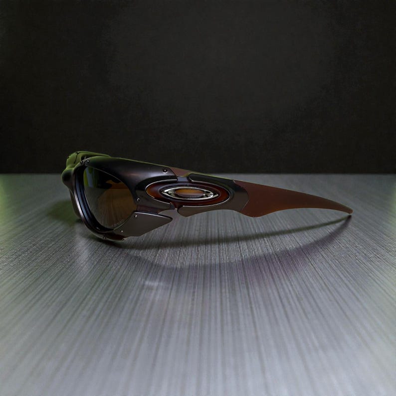 May include: A pair of Oakley sunglasses with a brown and black frame and tinted lenses. The sunglasses have a sleek, modern design with a curved shape and a metallic accent on the side. The lenses are a gradient brown color.