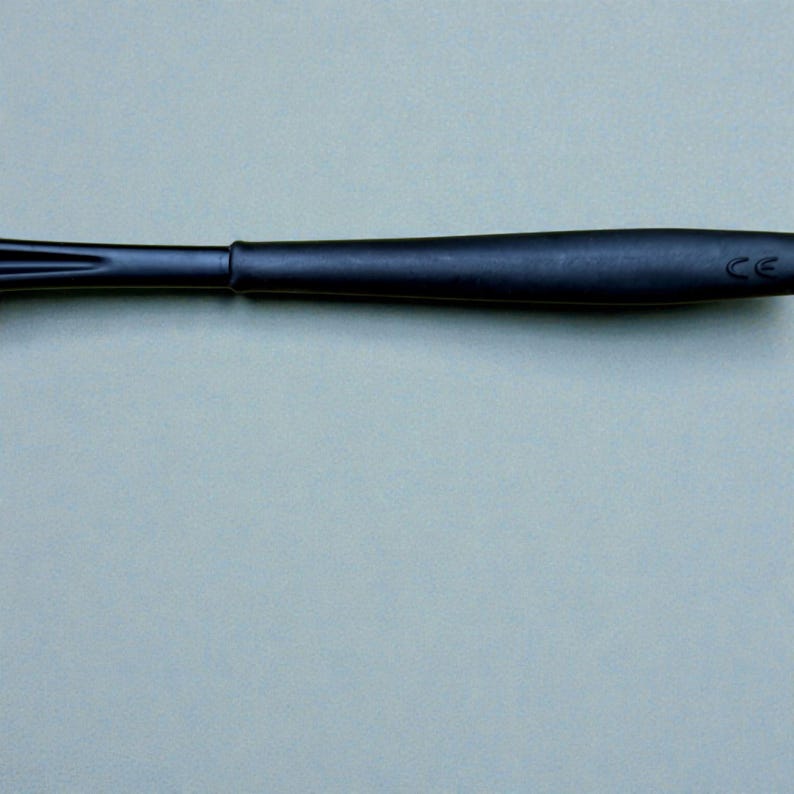 K&ouml;nnte beinhalten: Nahaufnahme eines schwarzen Utensils, m&ouml;glicherweise eines K&uuml;chenwerkzeugs. Das Objekt hat einen langen, schlanken Griff und ein breiteres, abgerundetes Ende. Die Oberfl&auml;che erscheint glatt und matt, mit subtilen Details.