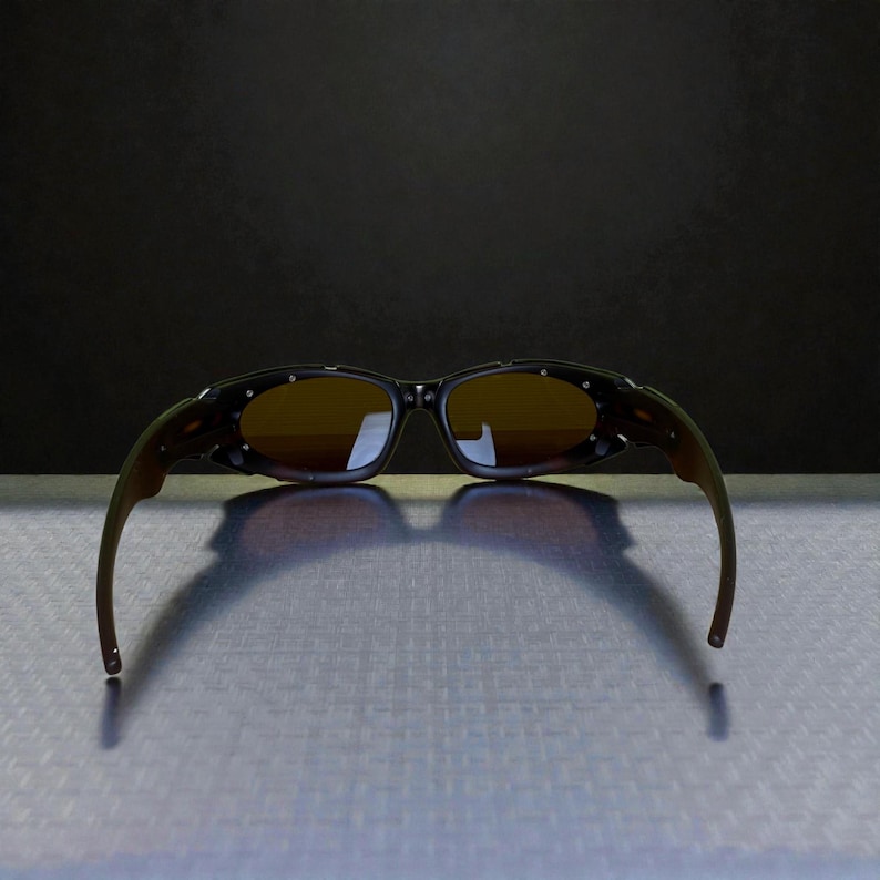 May include: Sunglasses with a dark frame and brown lenses. The sunglasses have a curved design with a dark brown and olive green color scheme. The lenses are a light brown color.