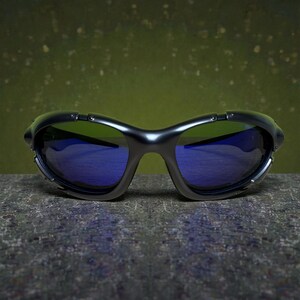 May include: Black sunglasses with blue lenses. The sunglasses have a curved frame and a sleek, modern design. The lenses reflect a blue hue, and the frame has a matte finish. The sunglasses are resting on a textured surface.