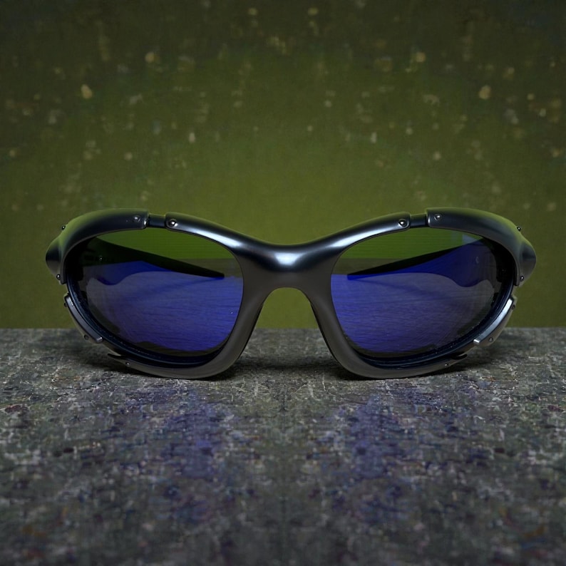 May include: Black sunglasses with blue lenses. The sunglasses have a curved frame and a sleek, modern design. The lenses reflect a blue hue, and the frame has a matte finish. The sunglasses are resting on a textured surface.
